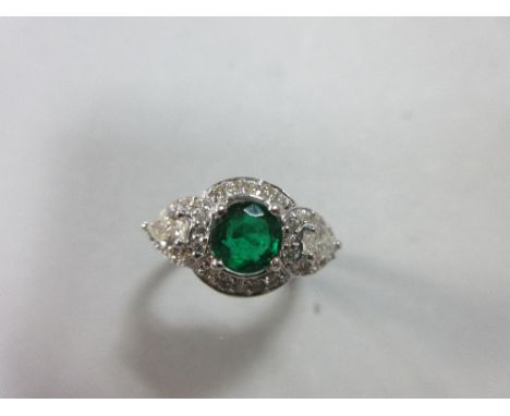 An emerald and diamond ring, the round cut emerald between two pear cut diamonds in overlapping borders of round brilliant cu