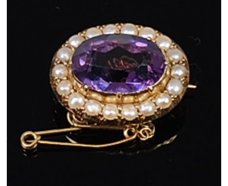 A yellow metal, amethyst and seed pearl set brooch, the illusion set oval cut amethyst measuring approx 15 x 10.5mm, in a sur