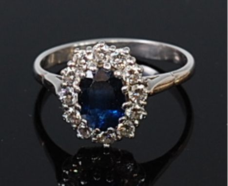 An 18ct white gold, sapphire and diamond cluster ring, the oval cut sapphire weighing approx 1.3ct, within a surround of twel