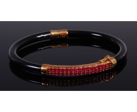 A black onyx 9ct gold and ruby set hinged bangle, arranged as two rows of fifteen round cut rubies, dia. 8cm