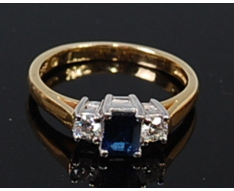 An 18ct gold, sapphire and diamond ring, arranged as a four claw set baguette cut sapphire weighing approx 0.4ct, flanked to 