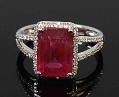 A contemporary 14ct white gold, ruby and diamond ring, the four claw set emerald cut ruby weighing approx 4.67ct, in a surrou