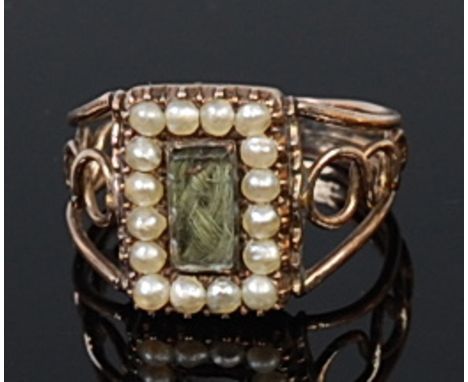 A late Georgian yellow metal and seed pearl set mourning ring, set with a plait of hair under crystal, the reverse with ename