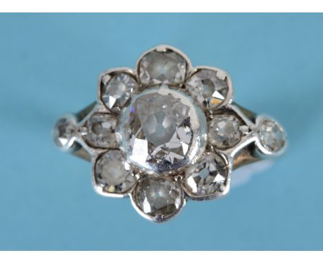 A Victorian diamond cluster ring, the large flowerhead flanked by two old brilliant cut stones, in a white and yellow coloure
