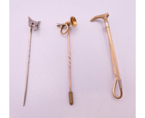 Two stick pins formed as a fox mask and a horn, and a brooch formed as riding crop. The latter 6 cm long.