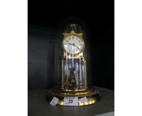 An early 20th Century brass torsion mantel clock with enamelled face, raised on a plinth base with glass dome.