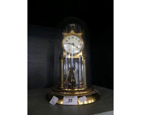 An early 20th Century brass torsion mantel clock with enamelled face, raised on a plinth base with glass dome.