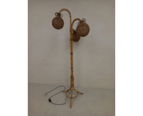 A 1970s retro floor standing bamboo lamp having three bent pendant arms with spherical woven wicker shades raised on splayed 