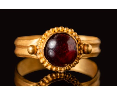 Ca. AD 500 - 600.A Byzantine gold ring with a round hoop and a central circular red cabochon on the bezel. The bezel is furth