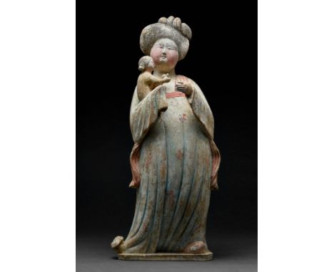 Ca. 618-906 AD. A Tang Dynasty terracotta lady holding an infant. The elegant figure stands on a flat base, with the head tur