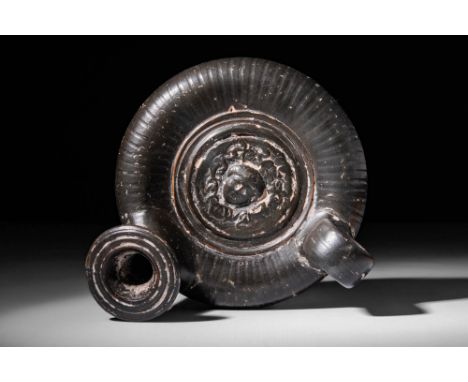 Ca. 400 - 300 BC.A Greek black glaze Guttus decorated on the top with a relief head of a Gorgons. The uniform and shiny black