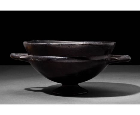 Ca. 6th-4th Century BC.A large, elegant black-glazed skyphos with a low pedestal disc foot and twin opposing handles. It is d