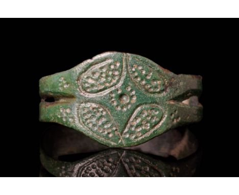 Ca. AD 1200 - 1400.A medieval bronze ring featuring a round hoop with a separated band. The bezel is adorned with two pairs o