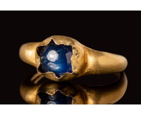 Ca. AD 1200 - 1400.A medieval gold ring with a blue sapphire cabochon, secured by a crimped outer bezel.Size: D:14.27mm / US: