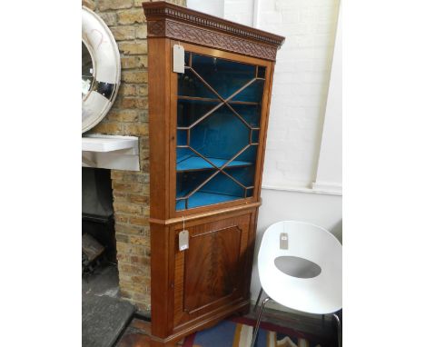 A George III style mahogany standing corner cupboard, the blind fretwork frieze above an astragal door enclosing a blue silk 