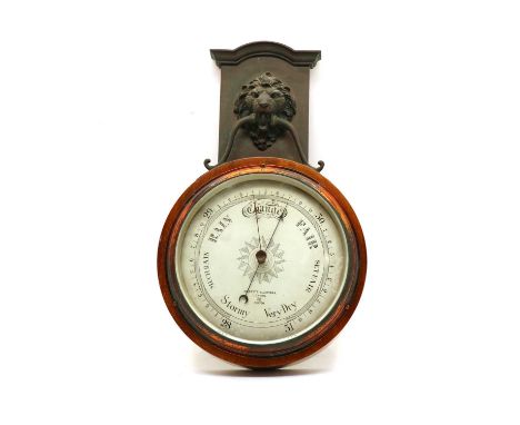 An aneroid barometer by Negretti & Zambra, the metal lions mask and bezel mounted on mahogany, label verso 'wood from HMS Emp