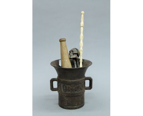 A cast iron mortar, a skull form nut cracker, a pestle and a baton. The former 15 cm high.