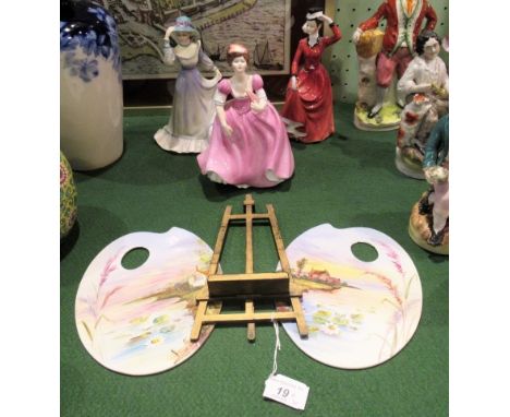 Two small ceramic artist's palettes, each decorated with a river landscape, together with a small giltwood folding easel, one
