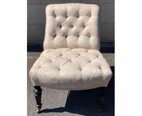 A Victorian button back nursing chair, standing on ebonised and reeded gilt legs 