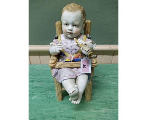 An early 20th Century continental biscuit porcelain figure of a seated child with rattle (small chips to toe and back chair l