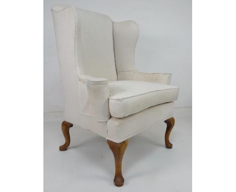A wing back armchair, with high back and outswept arms, raised on cabriole legs, recently upholstered in cream fabric, 91 by 