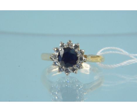 An 18ct gold sapphire and diamond cluster ring, the round sapphire in claw setting with twelve brilliant cut diamond border, 