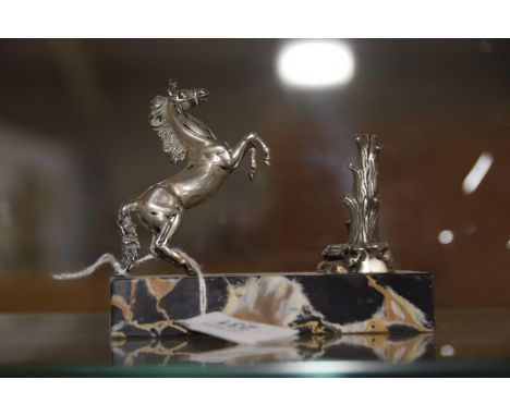 A 1930's white metal desk ornament, modeled as a rearing horse in front of a tree trunk cast with a coiling snake, upon a rec