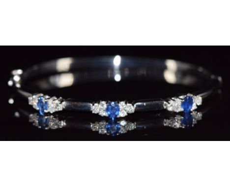 An 18ct white gold bangle set with three oval cut sapphires, each approximately 0.3ct and eighteen round cut diamonds, with i