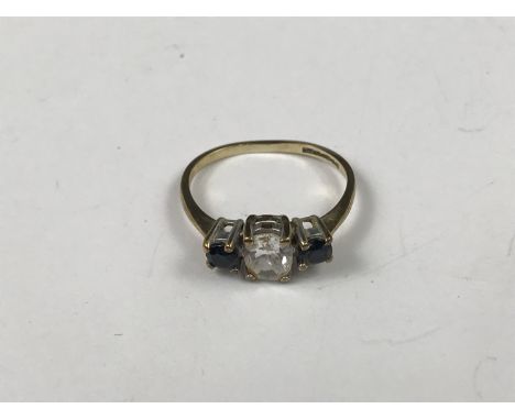 A 9ct gold three-stone dress ring, having a central oval-cut clear stone flanked by a pair of sapphire blue coloured stones 