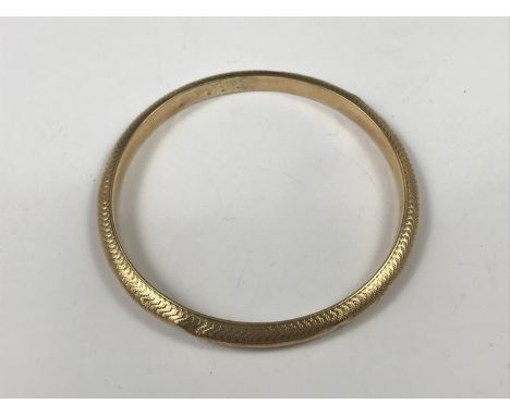 A yellow metal bangle, having engine-turned decoration, tests as gold, 10.6g