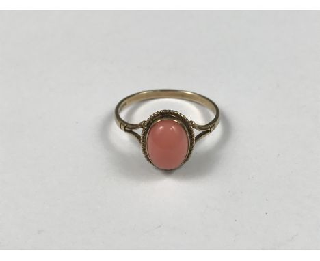 A 9ct gold and coral dress ring, the cabochon stone being rub and rope-twist set above a fine shank with bifurcated shoulders