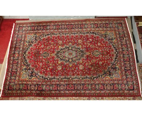 A large red ground Persian Mashhad carpet with traditional medallion design 290 x 196 cm.