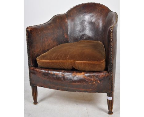 A vintage 20th Century Art Deco well weathered brown leather club armchair / fireside lounge chair having a shaped backrest w