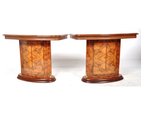 A pair of Hollywood Regency faux figured walnut console tables comprising of a shaped table top with central pillar having gi