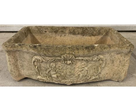 A stone trough style garden planter with carved cherubs and floral detail to front.  Drainage hole to base.  Approx. 20 x 54 