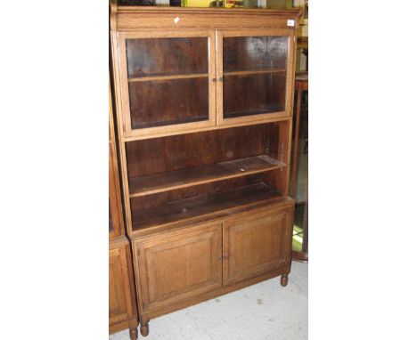 Early 20th Century oak bookcase with undershelf and blind panel cupboards on turned legs.