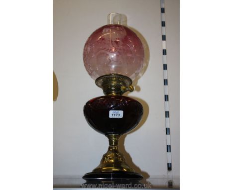 A brass oil lamp having a red reservoir and cranberry glass shade with two wicks.