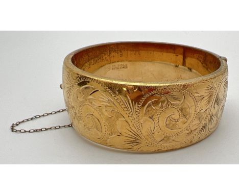 A vintage 9ct gold metal core hinged bangle with half floral engraved pattern, push clasp &amp; safety chain. Marked to insid