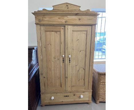 An antique pine 2 door wardrobe with central drawer and shaped top. Ceramic knob handles and decorative metal key escutcheons