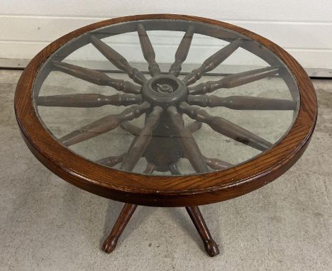 A vintage dark wood and glass topped coffee table made from a spoked wheel. Approx. 42cm tall x 75cm diameter. 