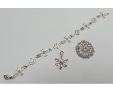 3 pieces of silver and white metal filigree design jewellery. A small flower shaped pendant, a bracelet with cross and twist 