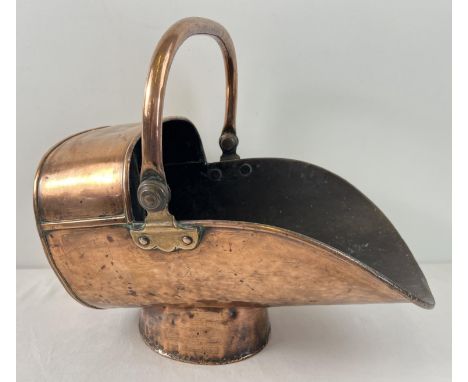 A Victorian copper and brass helmet fireside coal scuttle with hinged swing handle. Raised on a cylindrical tapering foot. Ap