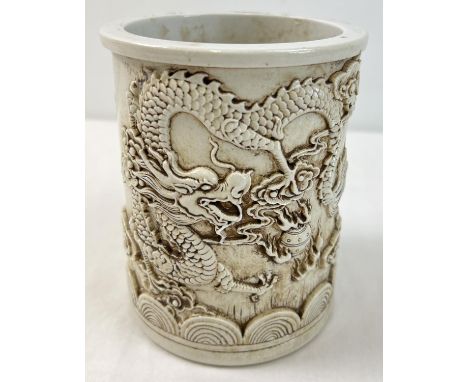 A Chinese white ceramic brush pot with dragon design shown in relief and shaped bottom rim. Impressed signature mark to under
