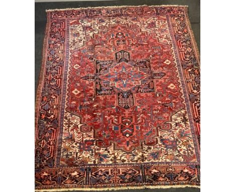 A hand woven Heriz carpet geometric designs in blue, cream and caramel on a red ground. 383cm x 273cm 