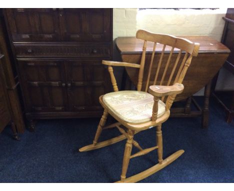 An oval oak gate leg table on turned supports, stick back rocking chair and a reproduction cocktail cabinet.