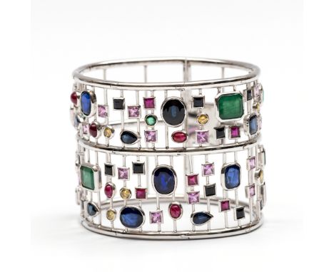 18 kt. Witgouden spang armband. Opgebouwd uit een rasterwerk, bezet met 7 smaragden (11.28 ct.), 12 blauwe saffieren (20.84 c