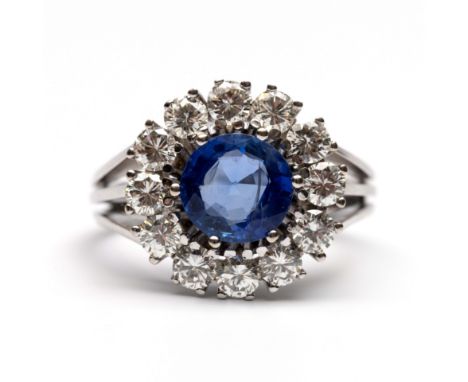 14 kt. Witgouden ring, centraal bezet met een gefacetteerde ronde blauwe saffier (diam. ca. 8 mm, ca. 1.74 ct.), in een entou