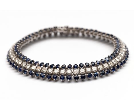 18 kt. Witgouden tennisarmband, bezet met twee rijen blauwe saffier waartussen een rij briljant geslepen diamant  met een tot