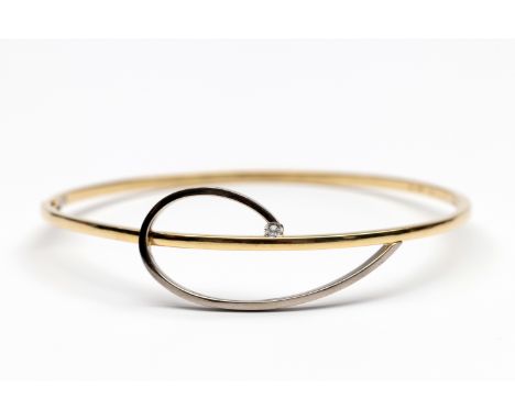14 kt. Gouden stijve armband. De voorzijde met een krullende baan in witgoud, uitkomend in een briljant geslepen diamant van 