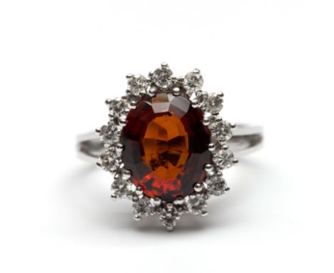 14 kt. Witgouden ring, centraal bezet met een ovale gefacetteerde bruinrode granaat (11 x 9 mm) in een entourage van briljant